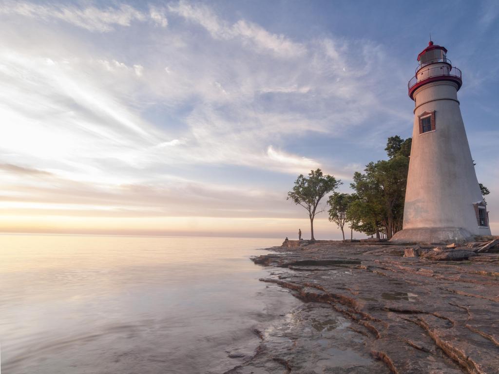 The Marblehead Lighthouse on the edge of Lake Erie in Ohio, USA taken at sunrise with a calm lake in the foreground.