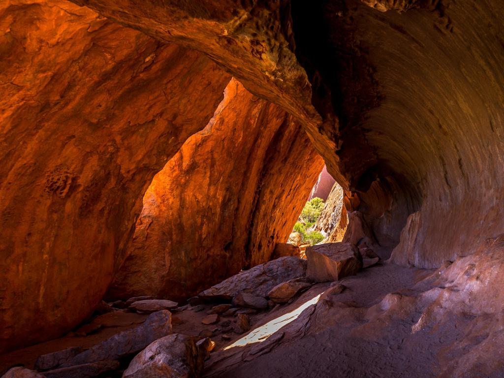 Uluru, Australia inside the base of a cave showing daylight through a gap in the distance.