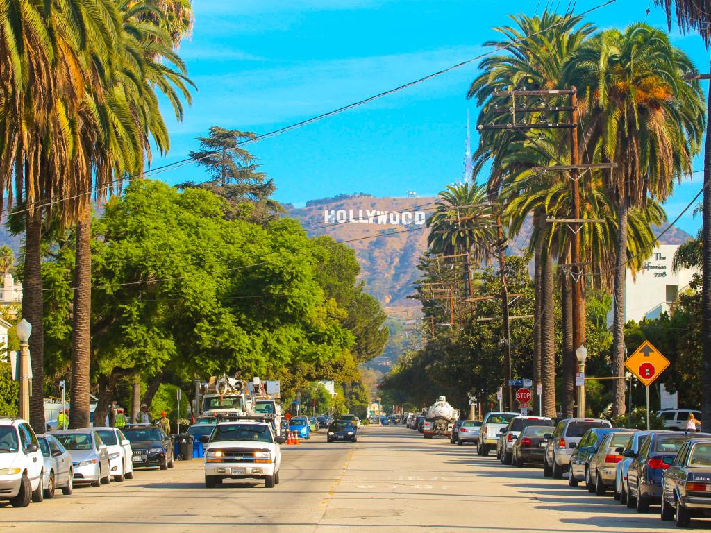 Beautiful Hollywood highway road with cars, palms and a sign on the hills. Clear blue sky.