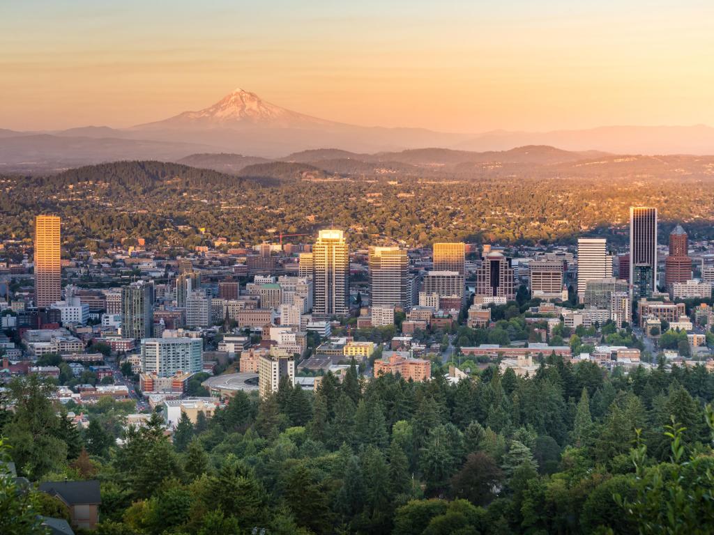 Downtown Portland, Oregon at sunset from Pittock Mansion. The photo shows the city shadowed by Mt. Hood as a backdrop.