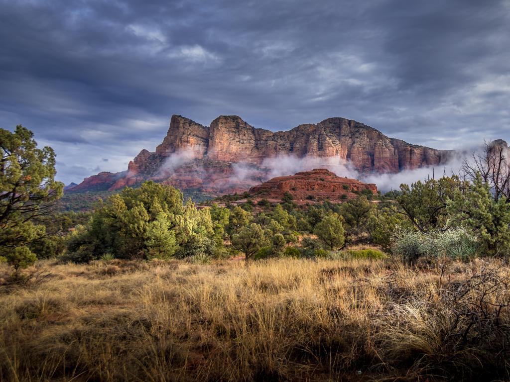 Mountain surrounded by low cloud with dark, stormy sky and grassy foreground