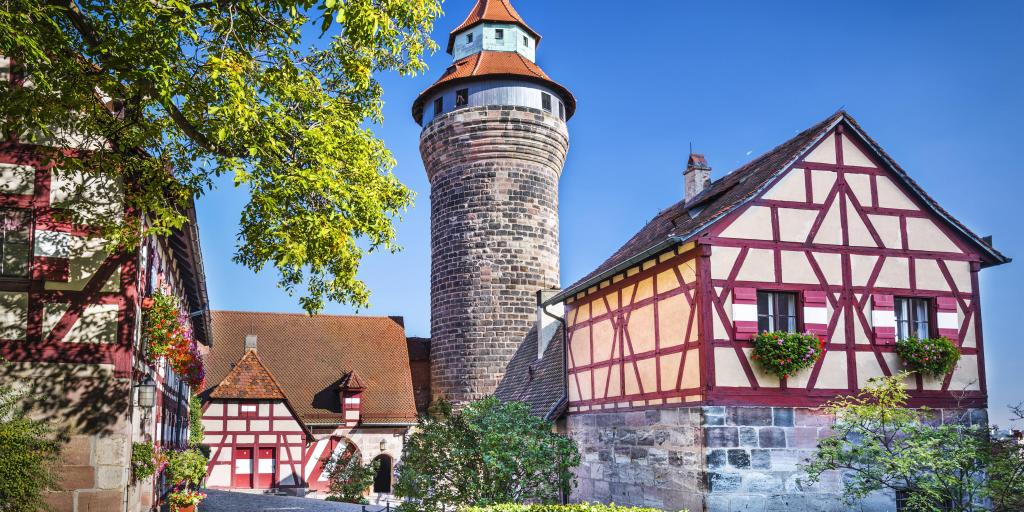 A round tower at Nuremberg Castle, Germany, flanked by two white and red half-timbered buildings, on a sunny day