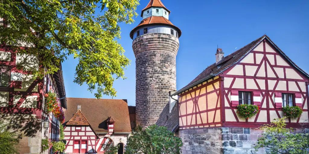 A round tower at Nuremberg Castle, Germany, flanked by two white and red half-timbered buildings, on a sunny day