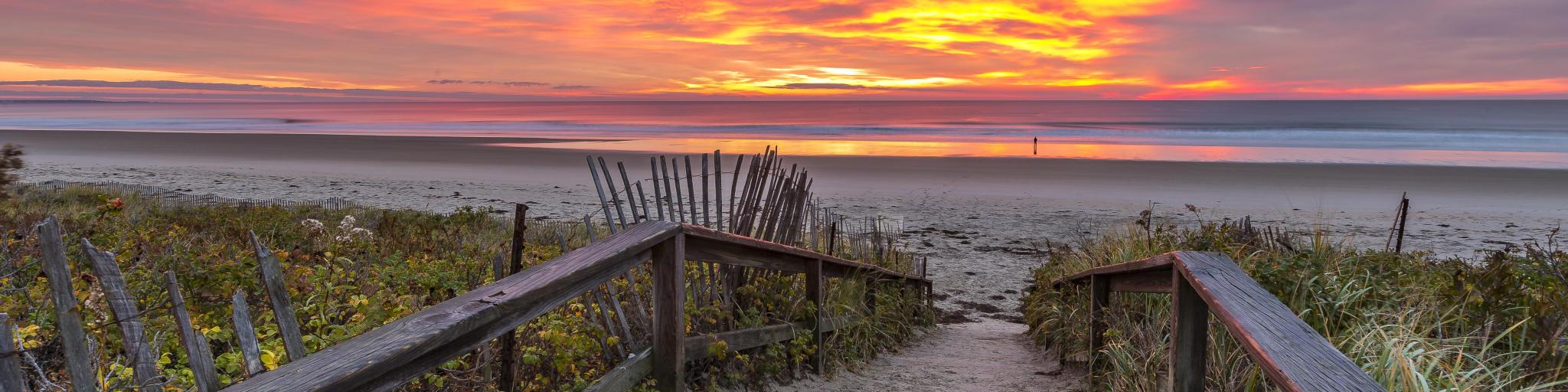 Board walk down to empty, wide, flat sandy beach with vibrant pink sunrise