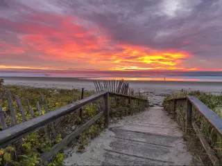 Board walk down to empty, wide, flat sandy beach with vibrant pink sunrise