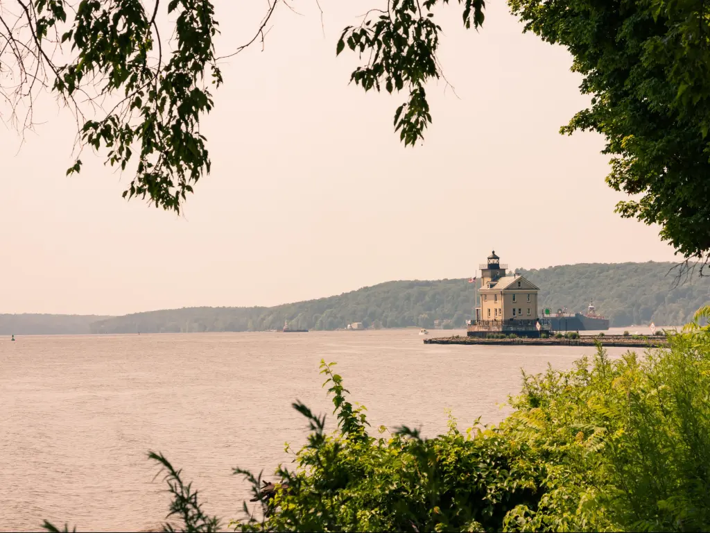 Rondout Lighthouse, New York, USA with the Hudson River in Kingston in the foreground and trees surrounding it.