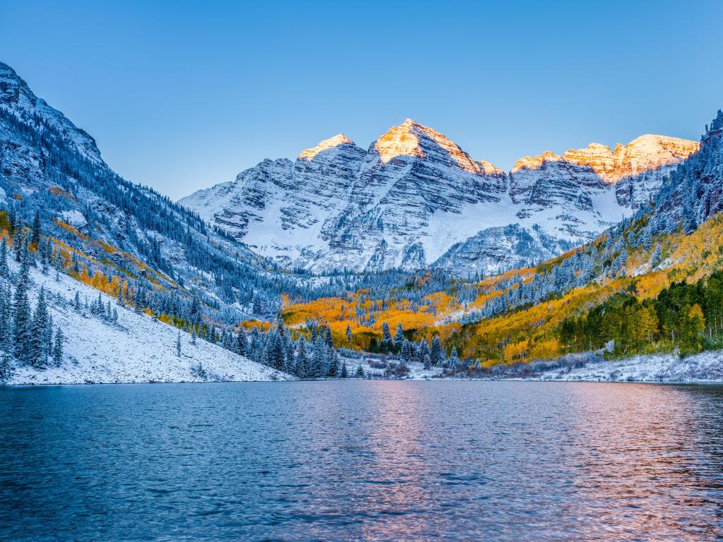 Aspen, Colorado, USA with Maroon Bells at sunrise in the distance and a lake in the foreground taken in winter with snow covering the land.