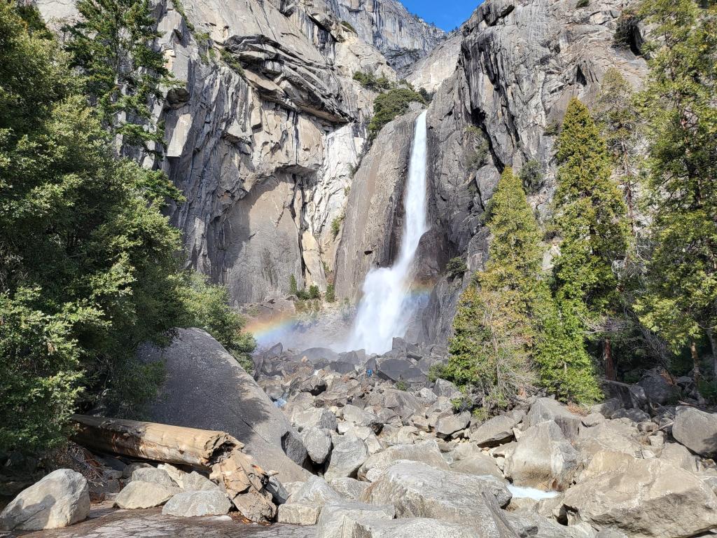 Waterfall creating a rainbow over the rocks, rocky trail to the viewpoint on a sunny day