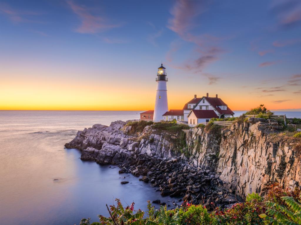 Portland, Maine, USA at Portland Head Light taken at sunset with green foliage in the foreground and the sea below the cliffs.