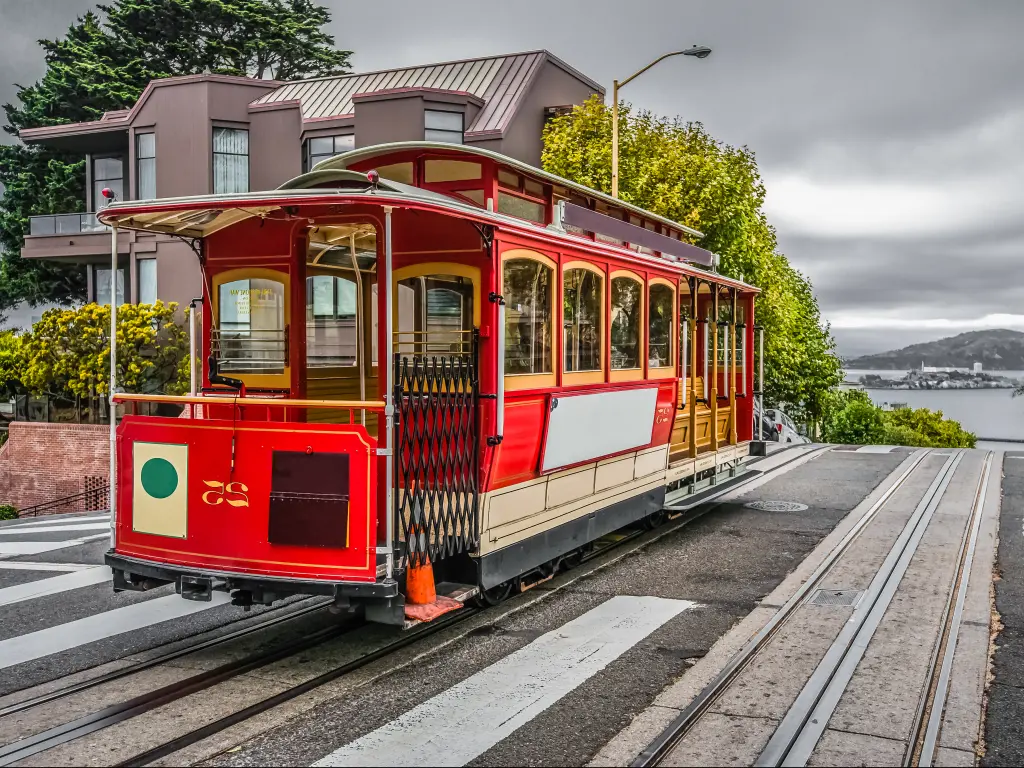 A bright San Francisco cable car on top of a hill with Alcatraz Island in the distance.