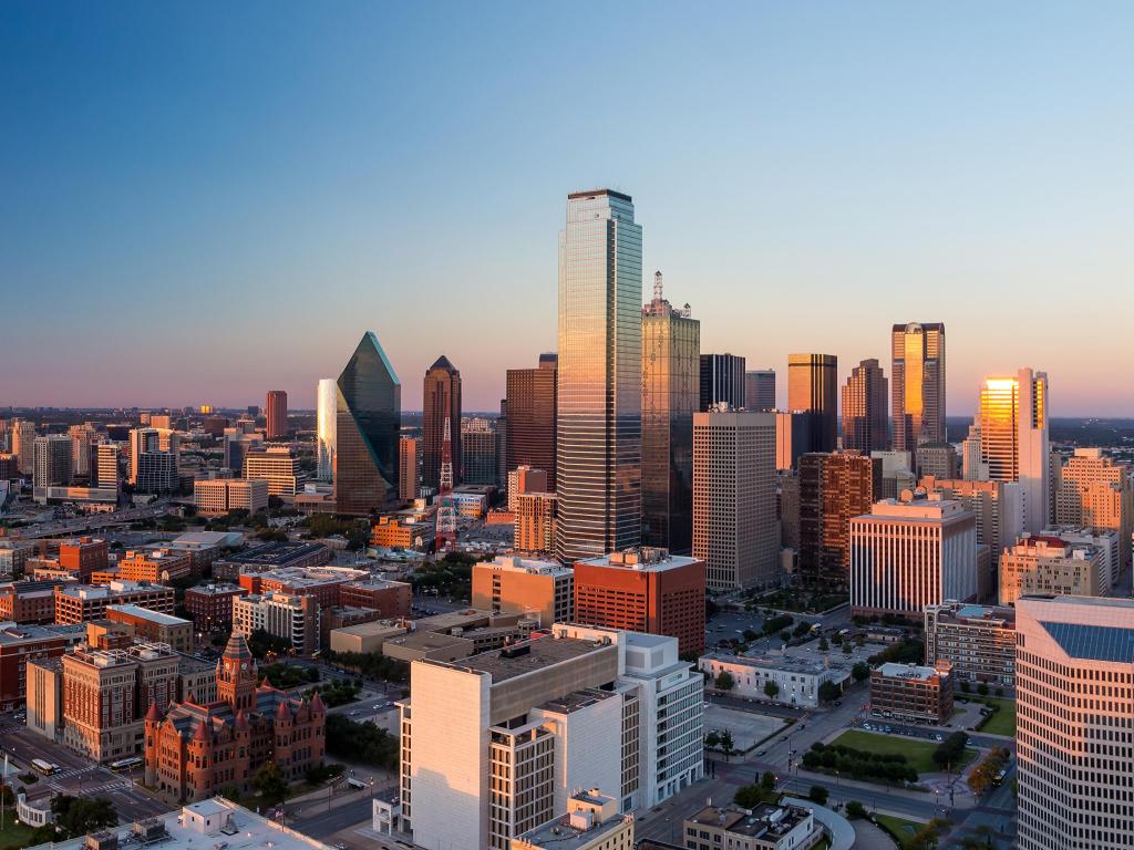 Cityscape with highrise buildings lit up with pink sunset light in blue sky 