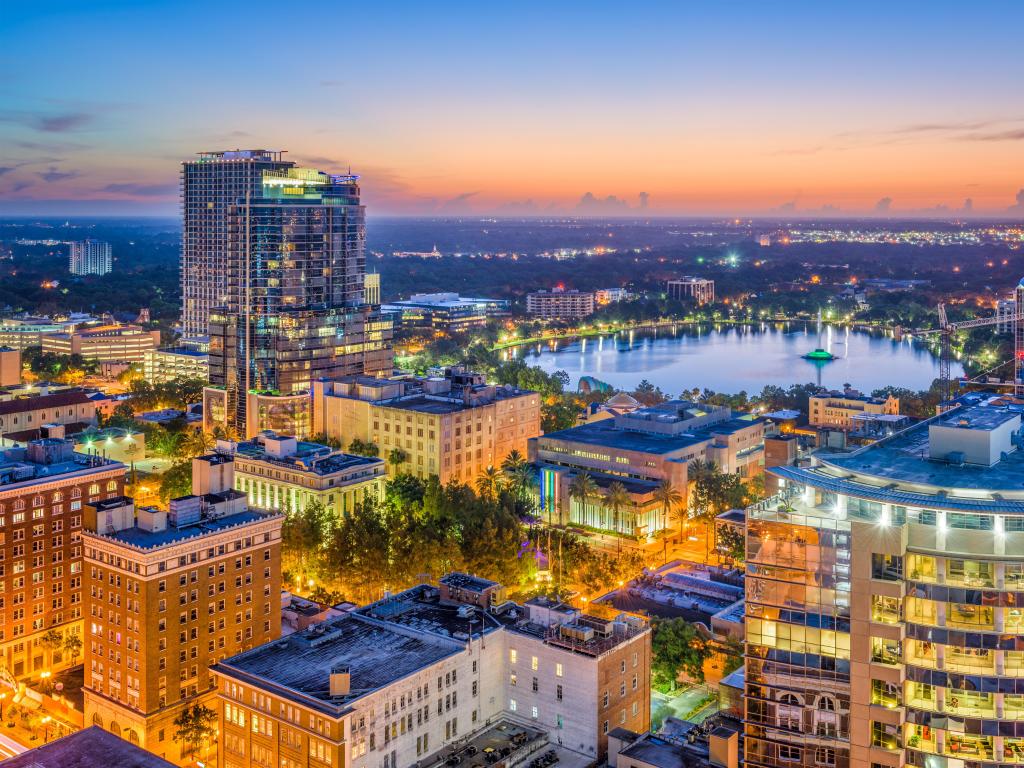 Orlando, Florida, USA with an aerial view of the skyline, city buildings in the foreground and Lake Eola in the distance at sunset.