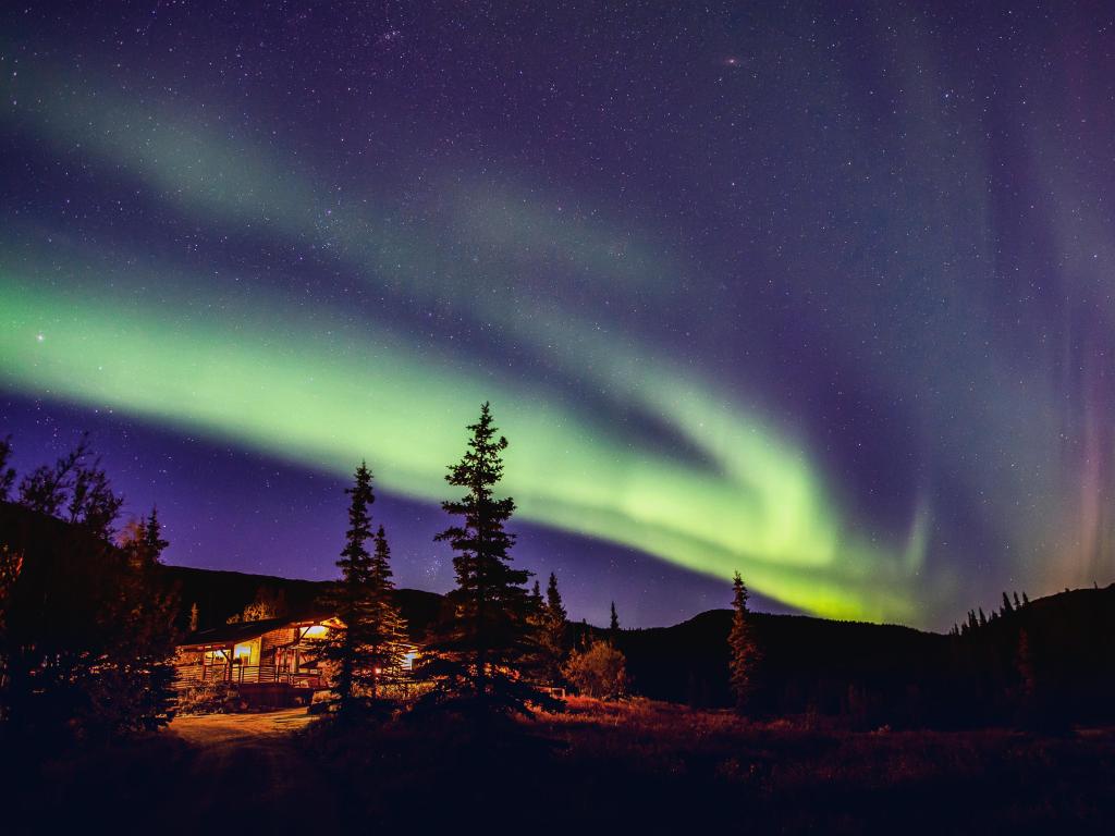 The Northern Lights shine over Denali National Park in Alaska. Green light shining above cabins 