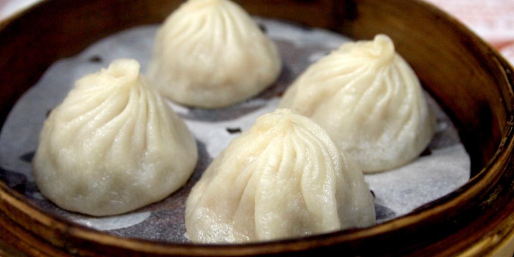 Four dim sum dumplings in a brown bamboo steamer