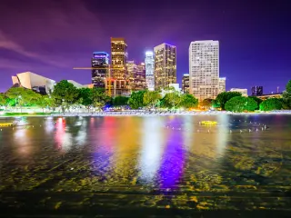 Los Angeles, California, USA downtown city skyline taken at night with the buildings reflecting in the water in the foreground.
