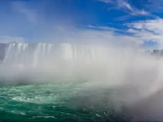 Panoramic view of massive, wide waterfall with white water cascading down into a turquoise splash pool, and a rainbow