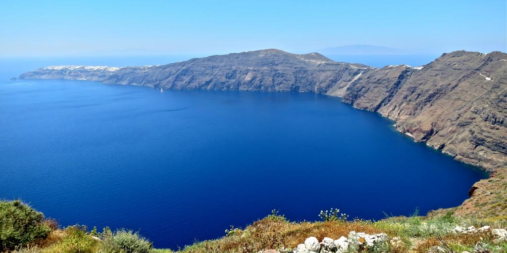 A view of the bright blue caldera in Santorini, Greece, from a high-up vantage point on a hike