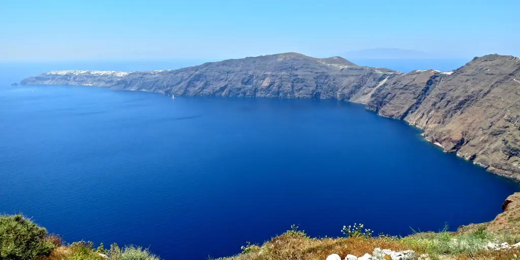A view of the bright blue caldera in Santorini, Greece, from a high-up vantage point on a hike