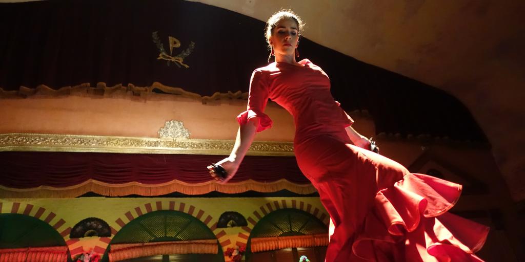 A flamenco dancer in a red dress dances on a stage in Sevilla