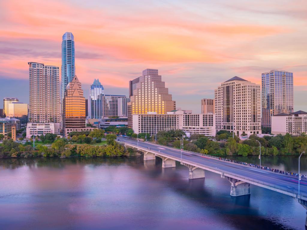 Bridge across wide river with sky scrapers on the banks, pink and gold sunset light