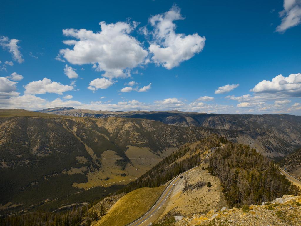 Aerial view view of winding Beartooth Highway amongst lush rolling hills and cloudy blue skies