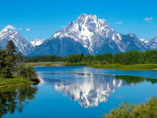 Snow capped mountains reflected in still lake water with pine trees