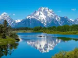Snow capped mountains reflected in still lake water with pine trees