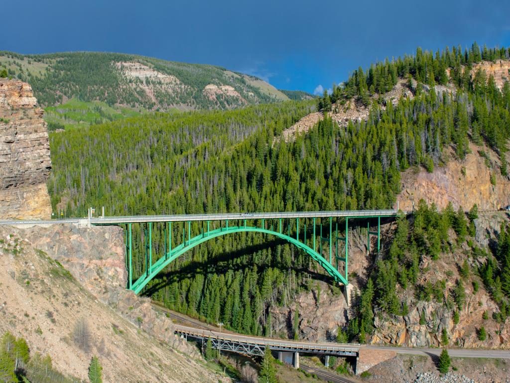 View of the green-colored Red Cliff Bridge spanning the gorge near Mintum, Colorado, with a blue sky above