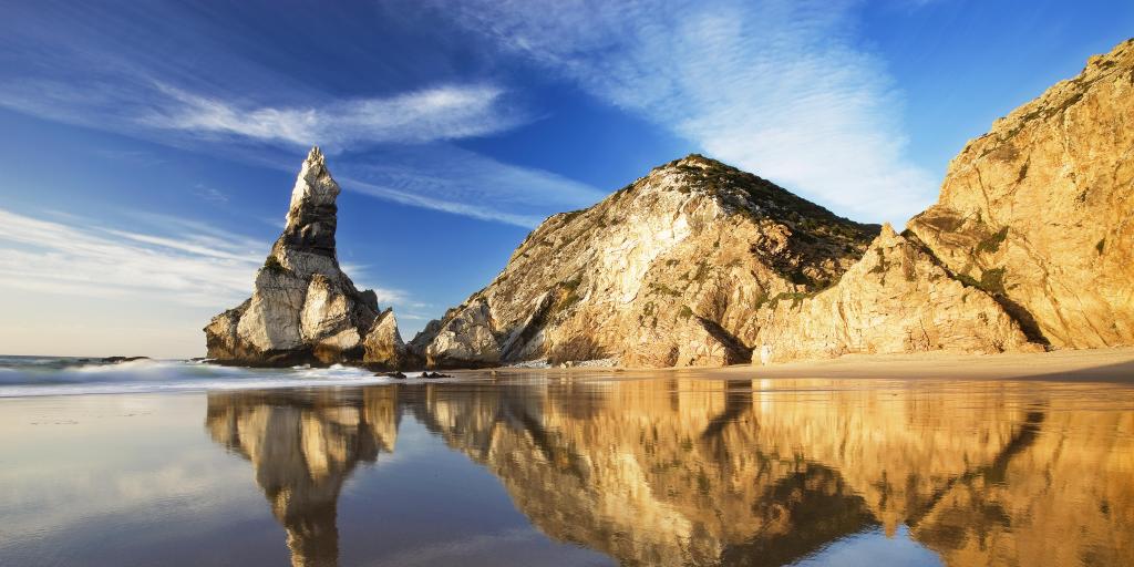 Rocks reflecting on the wet sand at Praia da Ursa beach, Portugal 