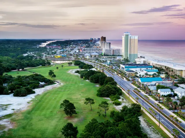 Panama City Beach, Florida, USA with a view of Front Beach Road at sunrise with greenery and trees on one side and the coast on the other.