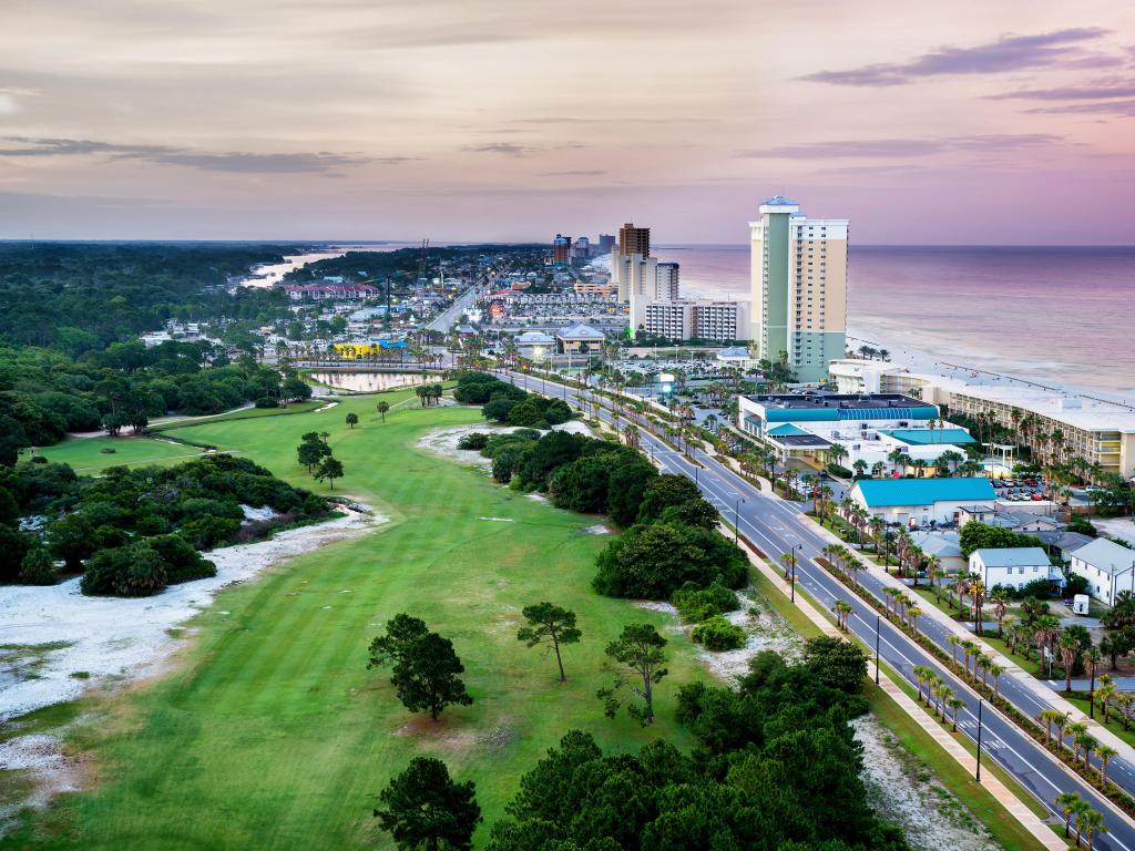 Panama City Beach, Florida, USA with a view of Front Beach Road at sunrise with greenery and trees on one side and the coast on the other.