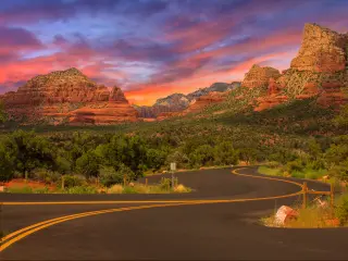 An image of an empty road in Sedona, Arizona during sunset with trees and a view of mountains.
