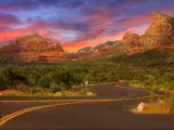 An image of an empty road in Sedona, Arizona during sunset with trees and a view of mountains.