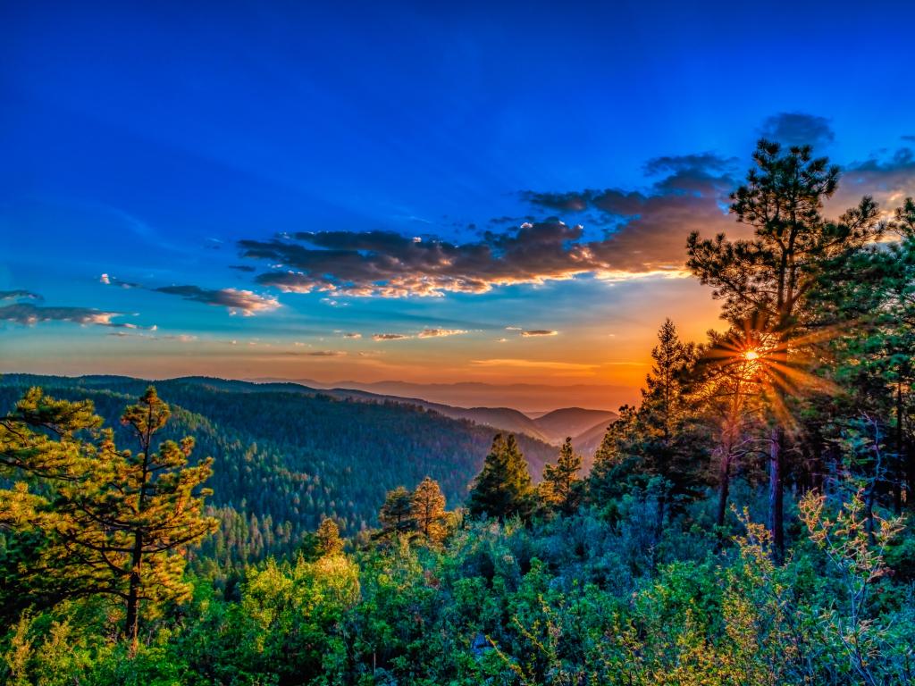 Sun sets with vivid colors thrown over forested mountain hillslope