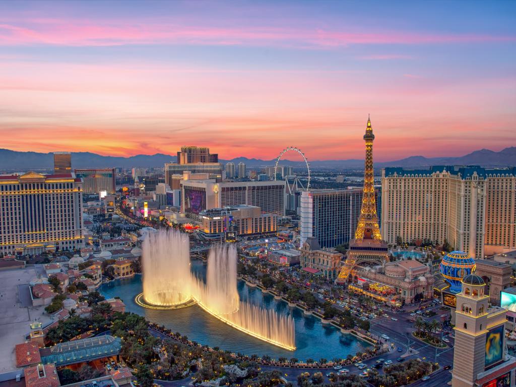 Illuminated view Bellagio Hotel fountains and Las Vegas strip during a colorful sunset.