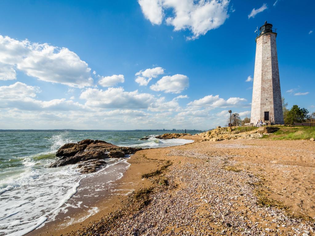 The New Haven Lighthouse, at Lighthouse Point Park in New Haven, Connecticut with sand in  the foreground, gentle sea and on a clear sunny day.