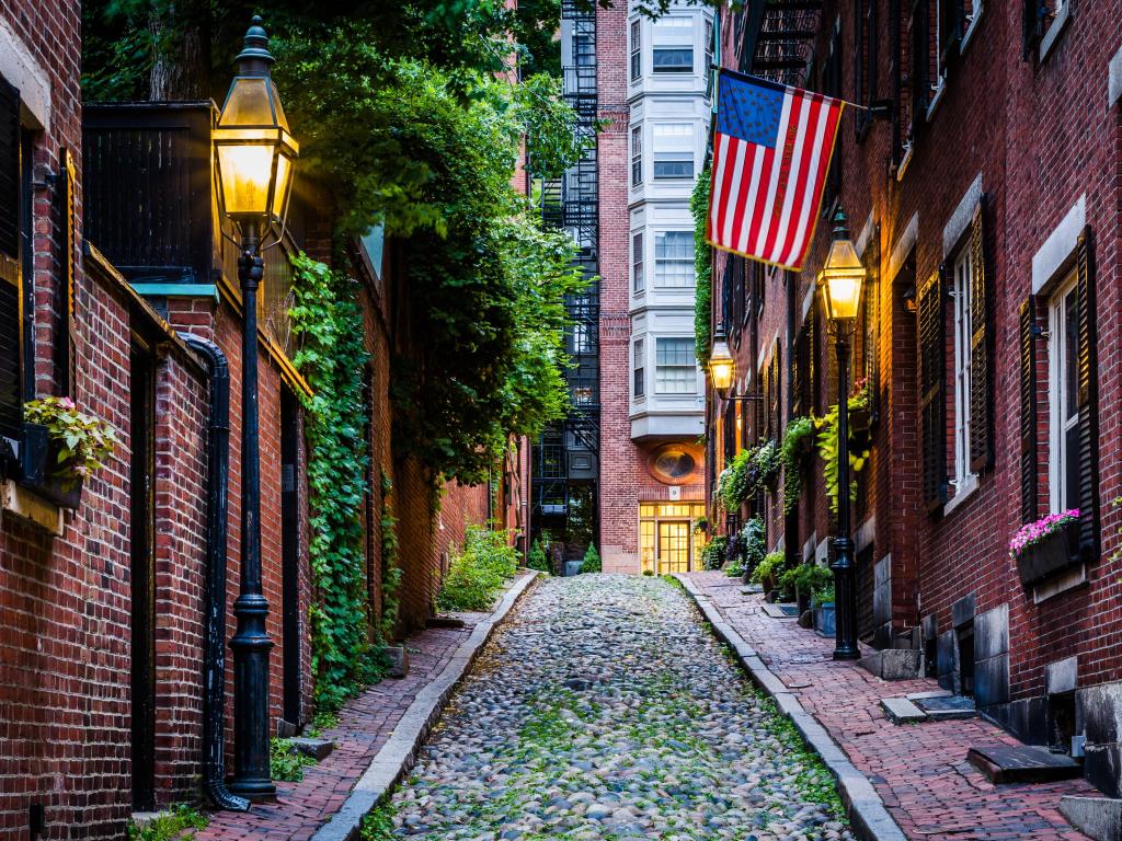 Cobbled street running up a hill with historic brick low rise buildings on either side and a US flag