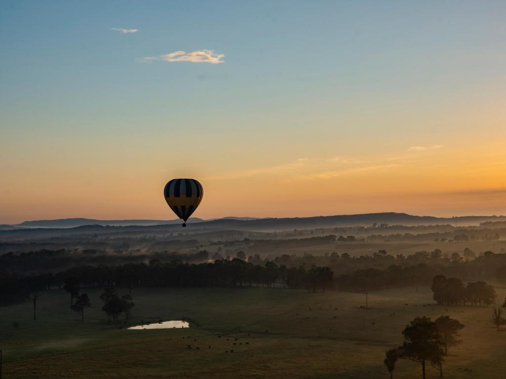 Hot air balloon over a misty landscape of green fields and trees at sunrise