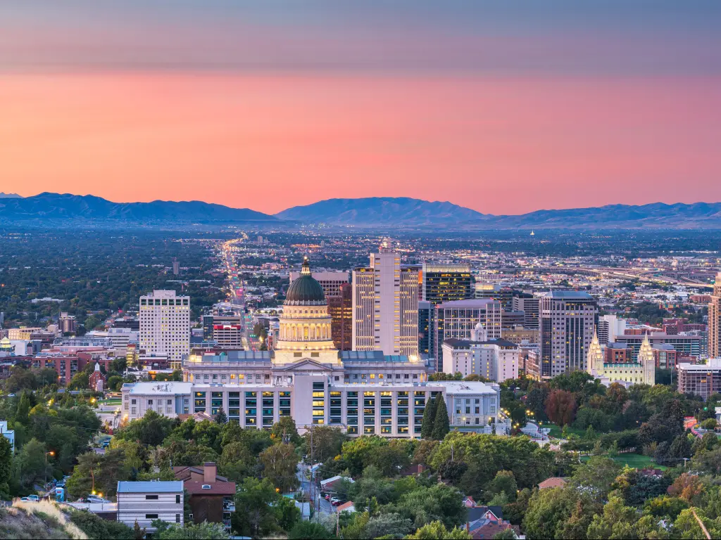 Salt Lake City, Utah, USA with a view of the downtown city skyline at dusk and mountains in the distance against a pink sky.