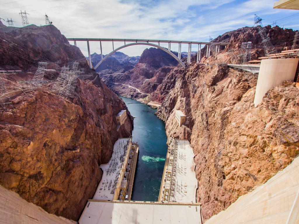 View over the Hoover Dam and Bridge in Nevada, with the red rocks either side and a cloudy sky above