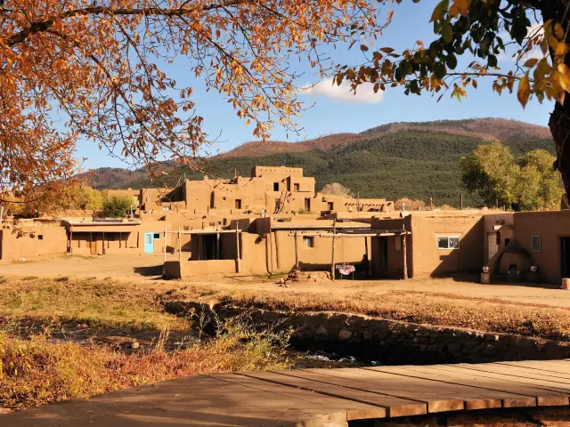 Red colored unique buildings of Taos, framed by autumn foliage