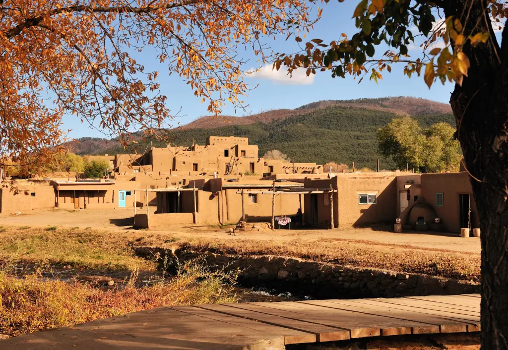 Red colored unique buildings of Taos, framed by autumn foliage