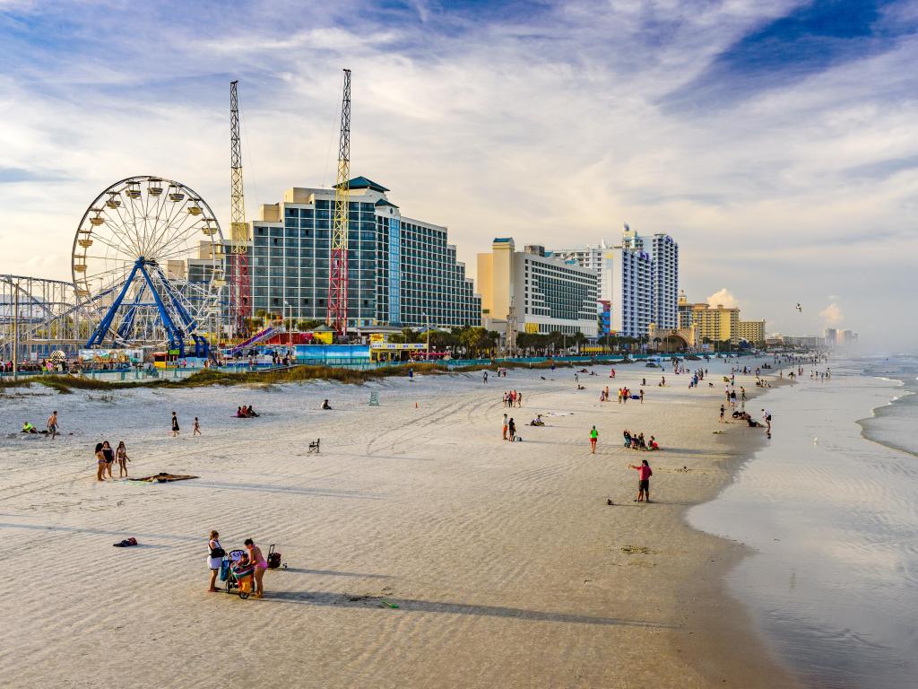 Aerial view of wide sandy beach with high rise buildings and ferris wheel under a lightly clouded sky