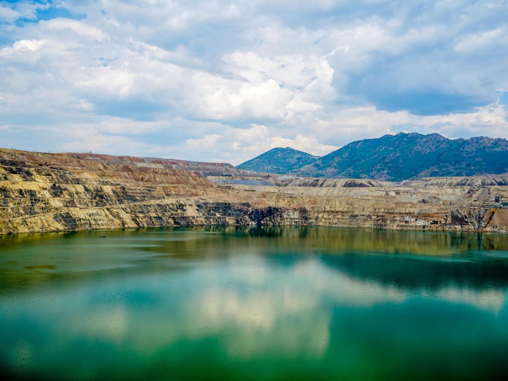 Toxic waters within the open pit at Berkeley Pit still make for an impressive sight, surrounded by steep hills and cloudy skies reflected in the pits water