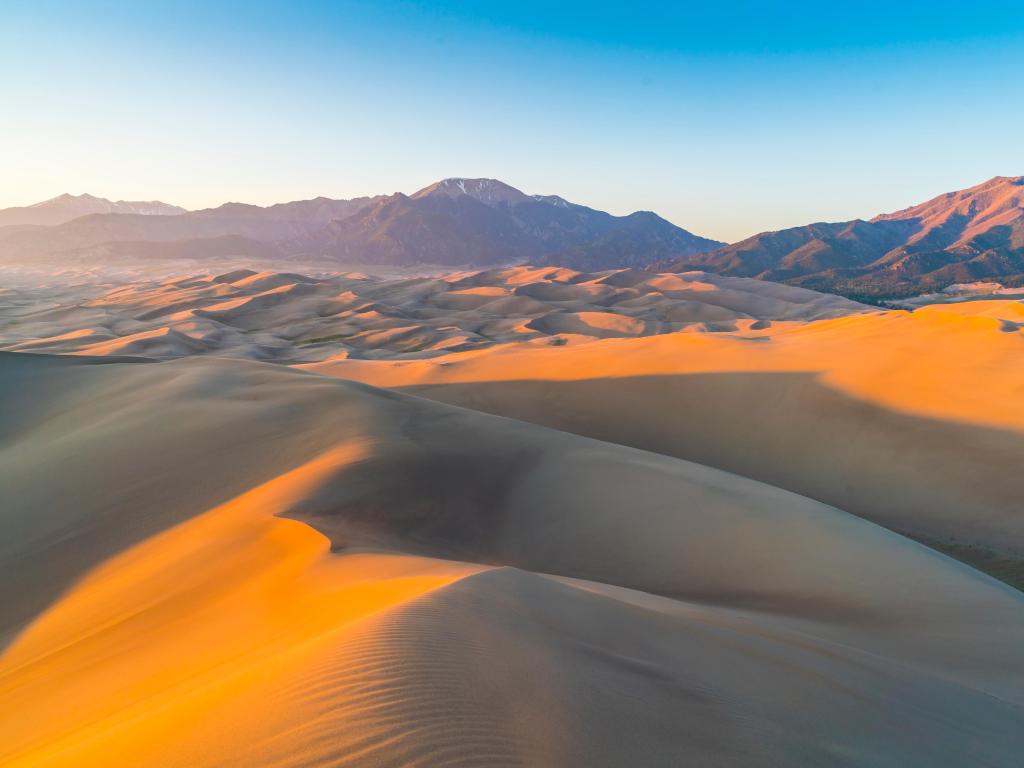 Great Sand Dune National Park, Colorado, USA at sunset with mountains in the distance and yellow sand in the foreground.