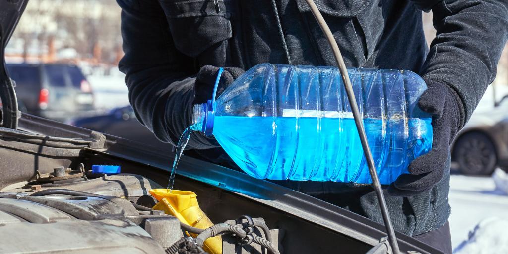 A person in gloves and a coat pouring antifreeze into a coolant system