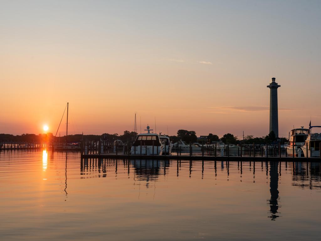 Rising sun reflects on calm lake water with silhouettes of small boats and jetties