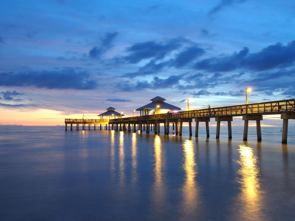 Fort Myers, Florida at sunset with the pier lit up and reflecting in the water below. 