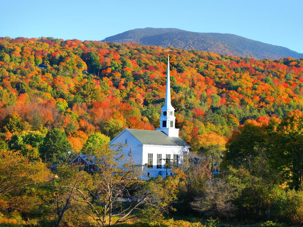 A white church amidst fall foliage on the trees, sunny weather