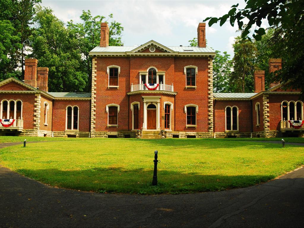 Red brick facade of the mansion with a front lawn, surrounded by trees
